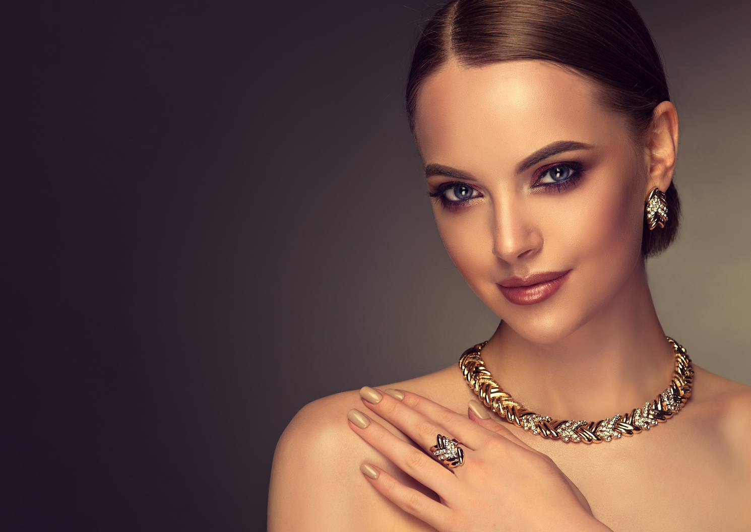 Pretty model with smoky-eyes makeup style is demonstrating gilded jewelry set.